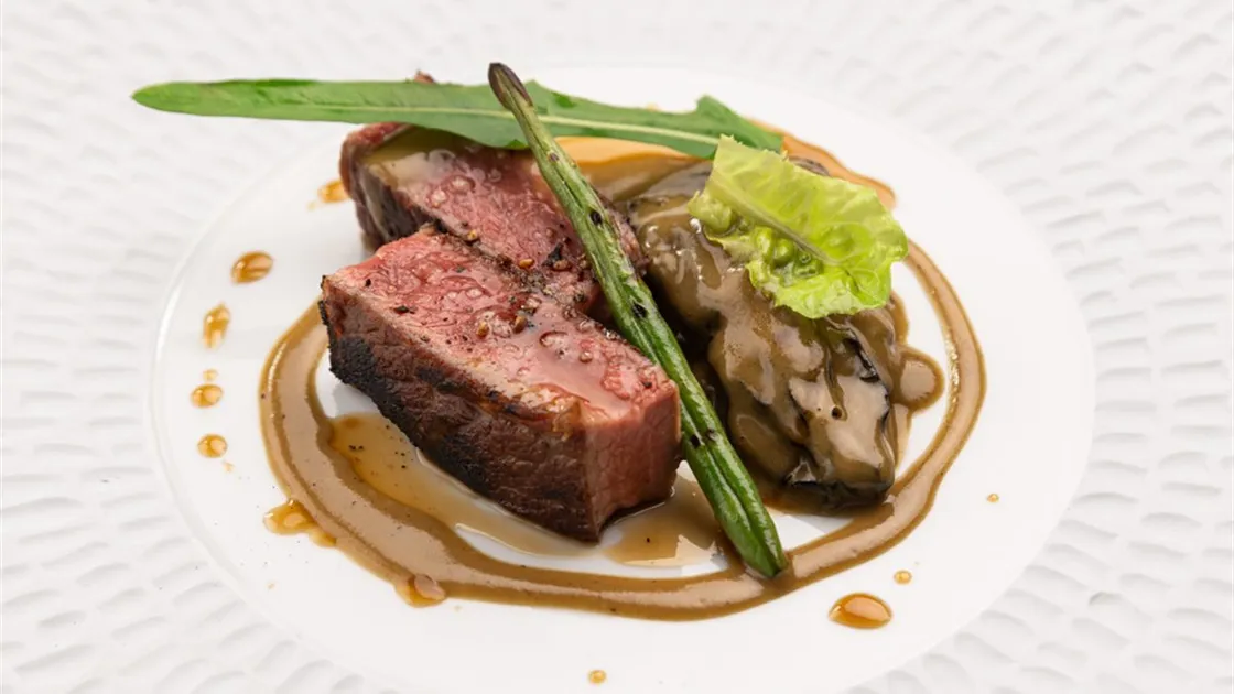 Entrecôte de wagyu do Picchi em duas fatias de interior rosado, com vagem grelhada, folhas verdes e molho escuro em prato branco
