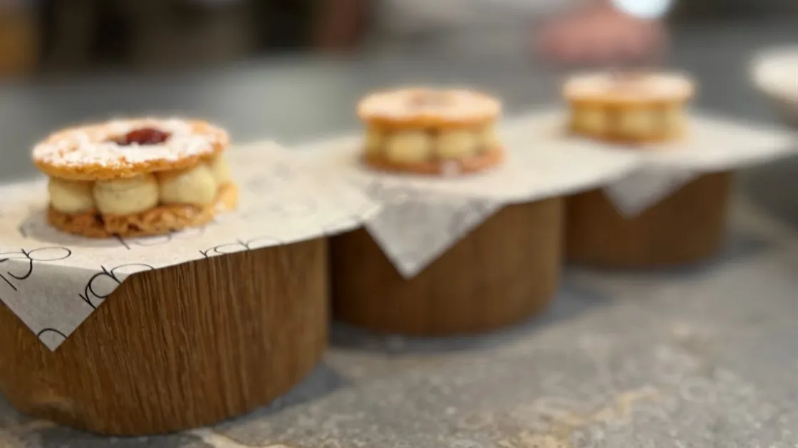 Três RSB Jammy Dodgers recheados de creme, servidos sobre bases de madeira com papel do restaurante