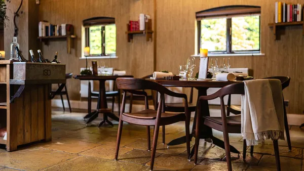 Salão do Restaurant Sat Bains, com mesas de madeira, piso de pedra e estantes de livros