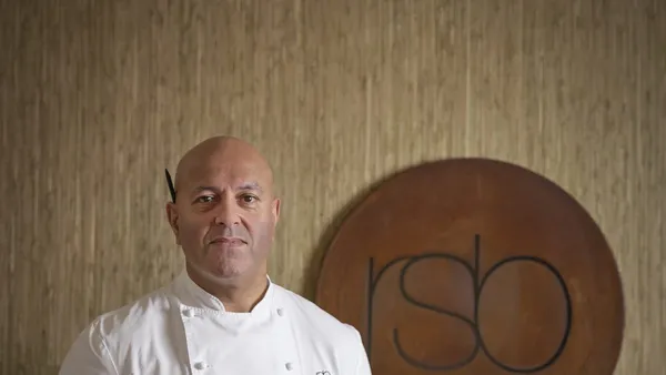 O chef Sat Bains, de dólmã branco, diante do logotipo RSB do restaurante