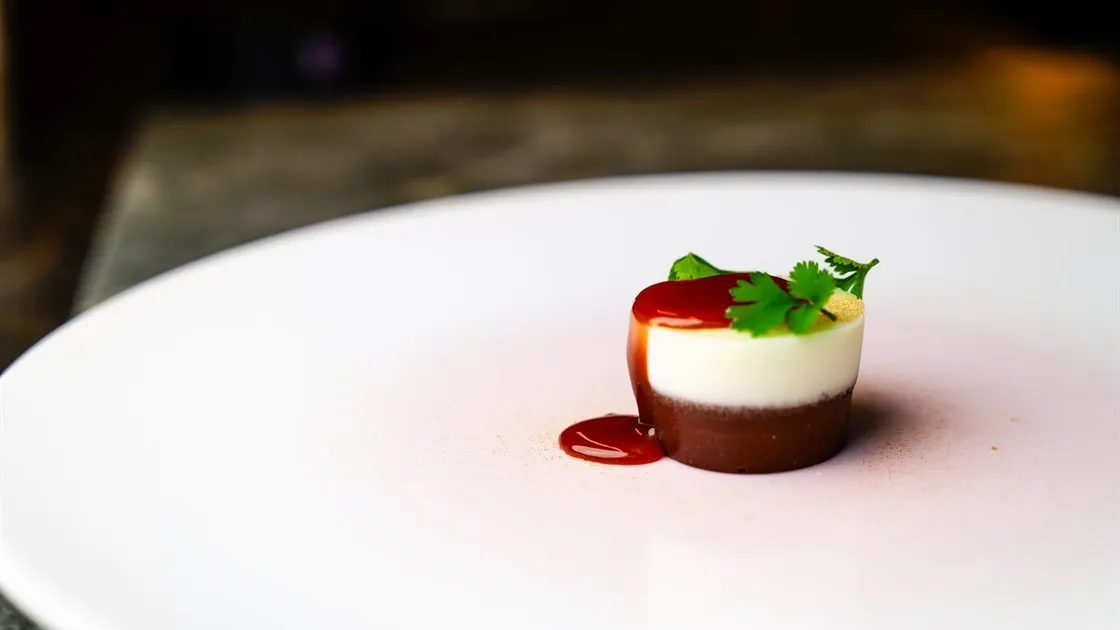 Sobremesa do Restaurant Sat Bains: camada de chocolate sob creme de iogurte, com folhas de coentro e um fio de calda, num prato branco