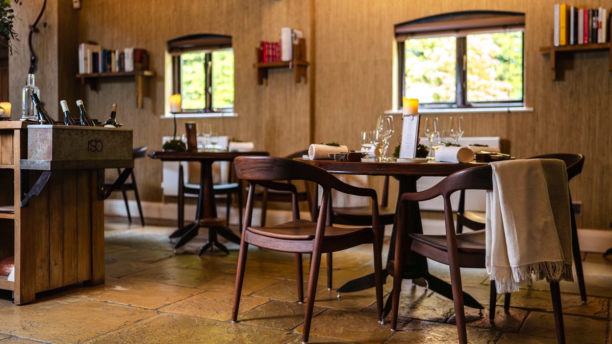 Salão do Restaurant Sat Bains, com mesas de madeira, piso de pedra e estantes de livros